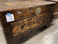 Front and side view of carved wood chest showing relief panels and brass latch.