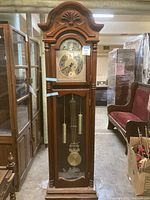 Full front view of the tall wooden grandfather clock in an indoor setting surrounded by other furniture and items.