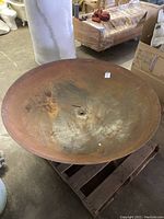 Full view of large round metal bowl with a rusted surface on a wooden pallet.