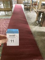 Photo showing the full length of long red narrow rug, displayed on a floor with some furniture in background.