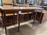 Full view of the long rectangular wooden table showing the tapered legs and polished wood finish with inlay details.