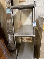 Metal shelf unit with three shelves stacked vertically and tubular metal legs.