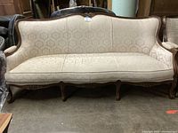 Front view of the ornate sofa showing the carved wood frame and damask upholstery in beige fabric.