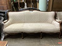 Front view of the ornate beige damask sofa with wooden carved frame and curved legs.