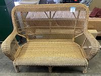 Front view of the used rattan sofa showing woven wicker seat, backrest, and curved armrests.