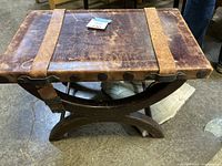 Top and side view of the accent table showing the leather top with two leather straps and metal studs, and the curved wood frame base.