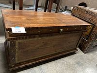 Full view of wooden chest showing carved edges and metal decorative accents on front panel.