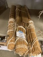 Photo of three rolled bamboo stick blinds or curtains tied with white ropes and secured with metal clips, showing natural light brown bamboo sticks.