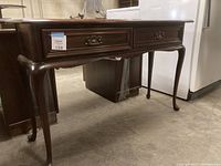 View of the wooden table from side showing two drawers and curved legs.