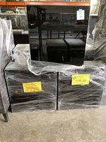 Two wrapped black wood upper cabinets with black glass doors, packed and stacked together.