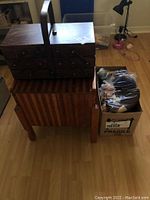Closed shot of the wooden sewing box, wooden utility box underneath, and a box of knitting wool beside.