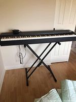 Front view of digital piano on adjustable X-style stand with power cable attached