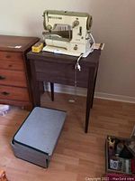 Bernina sewing machine on wooden sewing table with metal travel case on floor.