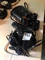 Pair of Bushnell zoom binoculars in leather case alongside Sony wireless headphones with cable, shown on table surface.