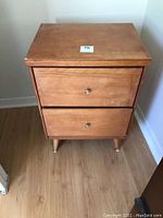 Front view of the wooden bedside table showing two drawers and metal knobs with surface scratches.