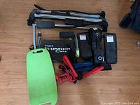 Photo of various exercise items on wooden floor including Cubii seated stepper, Wonder Core ab machine, balance board, small dumbbells, and other accessories.