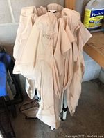 Folded gazebo frame and canopy bundled in beige fabric, standing against concrete wall.