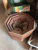 Wooden octagonal planters nested, green wheelbarrow with Scotts Turf Builder fertilizer bag inside, and metal garden stake reading 'Grandma's Garden'.