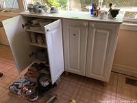 Front view of white kitchen cabinet with two doors open, displaying interior shelves with kitchenware and other items on top and inside.