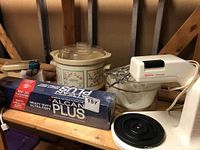 Crockpot slow cooker, Sunbeam Mixmaster electric hand mixer on a glass bowl, box of Alcan Plus aluminum foil, and Philips electric sharpener on wood shelf