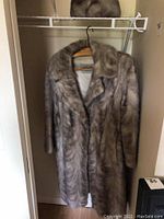 Full view of the light gray fur coat hanging on a wood hanger in a closet.