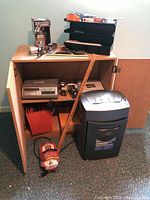 Plywood cabinet doors open revealing black Royal paper shredder on floor, Doufone answering machine inside cabinet, assorted office supplies on top and inside, wooden ruler leaning against cabinet.