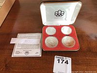 Open black leatherette case with red velvet insert showing four coins and certificate card.