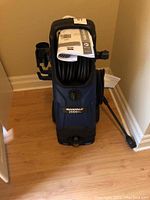 Front view of Simoniz pressure washer with hose reel, pressure wand and user manual on top
