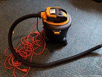 Full view of the Shop Vac with coiled orange extension cord on floor alongside the vacuum's black plastic hose.