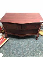 Front view of small wooden dresser with three drawers and cabriole legs on carpeted floor.