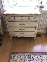 Full view of the dresser showing cream wood veneer with bronze detailing, three drawers, and ornate bronze handles.