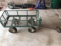 Full side view of the green metal yard wagon with mesh construction and pull handle, showing overall structure and condition.