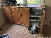 Full view of wooden kitchen cabinet with doors closed and one door open revealing interior shelves holding kitchenware and appliances.