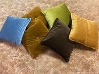 Six velvet throw pillows in various colors arranged on carpet, showing colors and sizes