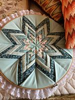 Close-up of round quilted star-pattern piece with delicate lace edging and floral fabric strips in green tones.