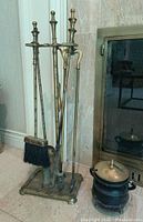 Full view of the brass fireplace tool set on stand with iron pot beside it