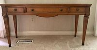 Full front view of walnut-finish console table with three drawers and fluted tapered legs.