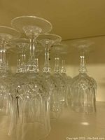 Fourteen crystal white wine glasses arranged upside down showing the cut and patterned stem and base.