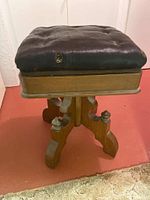 Front angled view of antique piano stool showing cushion with wear and carved wood base.