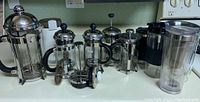 Wide view showing all French presses, mugs, and coffee grinder lined up on countertop