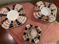 Photo showing Royal Castle dish set with stacked plates, bowls, and a teacup on a pink cloth surface.