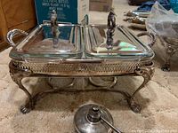 Side view of sterling silver plated double rectangular chafing dish with ornate claw feet and two lids. Oil burner positioned in front.