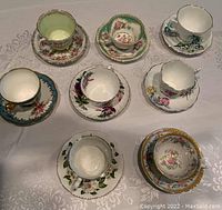 Top view of seven porcelain teacups with matching saucers featuring floral patterns and gold accents