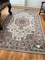 Full view of the large rectangular area rug on hardwood floor, showing central floral medallion and border pattern.