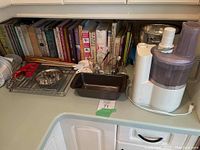 Overview of baking cookbooks, food processor, metal baking pan, mixing bowls, and kitchen utensils on countertop.