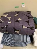 Purple duvet with abstract pattern on top of blue and white striped sheets.