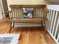 Front view of the solid wood bench with floral cushion, showing the full bench with armrests, turned legs, and wooden slat backrest.