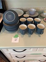 Photo showing the full set of Colorwave by Noritake blue dishes including plates and six blue mugs, with two small purple bowls visible. Items show used condition with some wear.