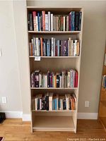 Full view of the entire bookcase placed against a wall, showing all shelves filled with books except the bottom shelf which is empty.