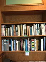 Photo of two wooden bookshelves with multiple rows of various sized and colored books in used condition. Titles including history and literature visible.